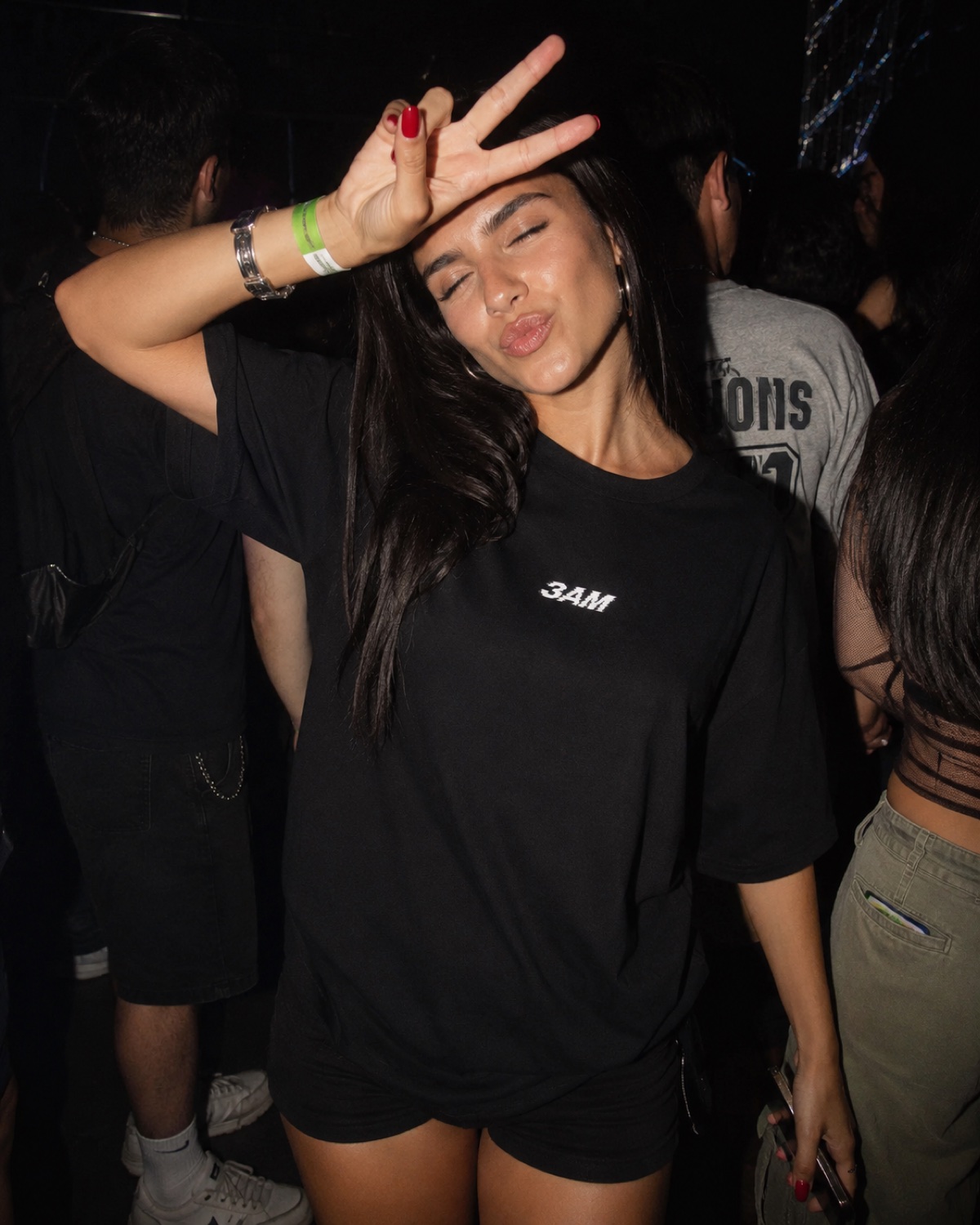 Woman in the 3AM tee throwing a peace sign at a club