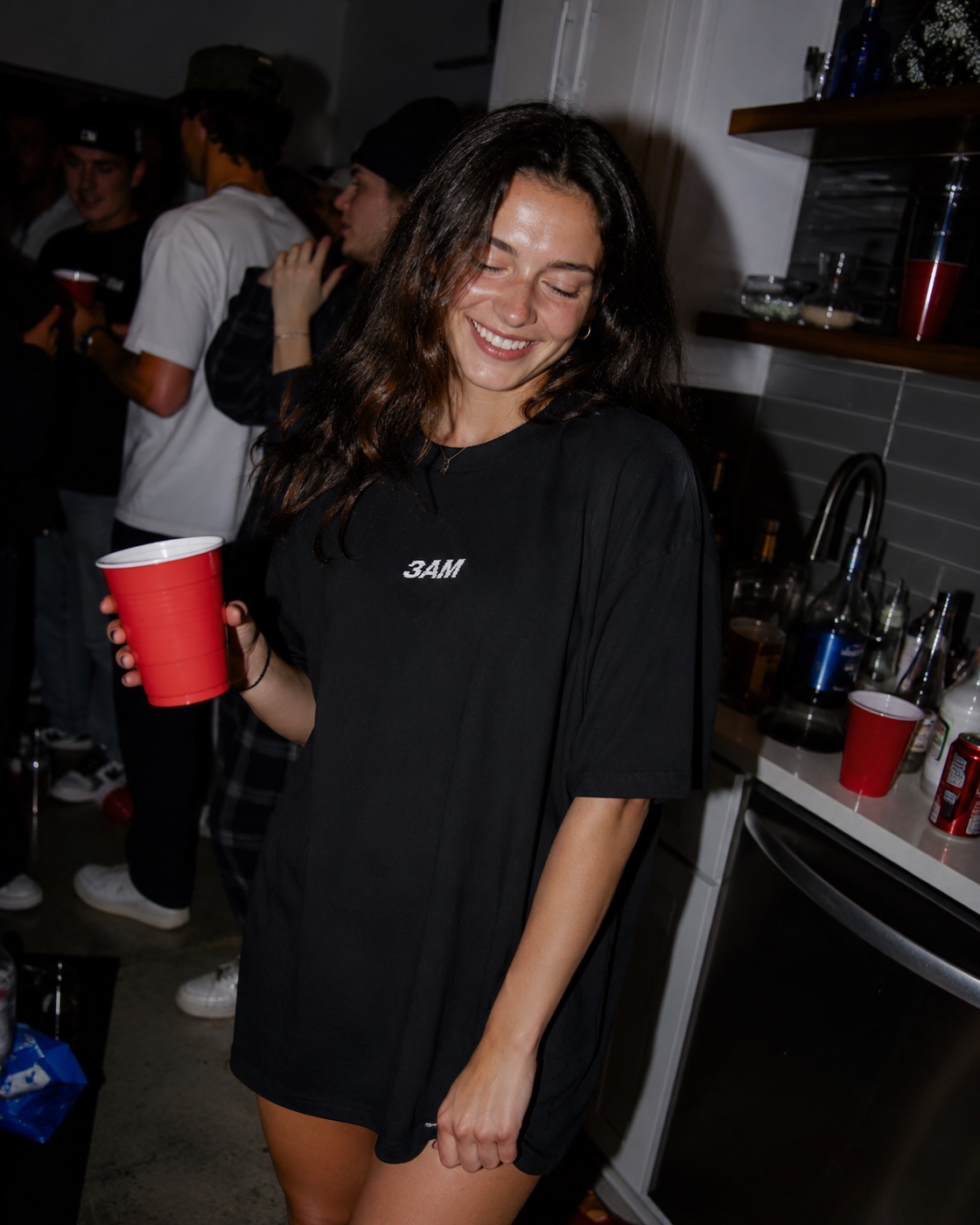 Woman in the 3AM Local tee holding a red cup at a house party