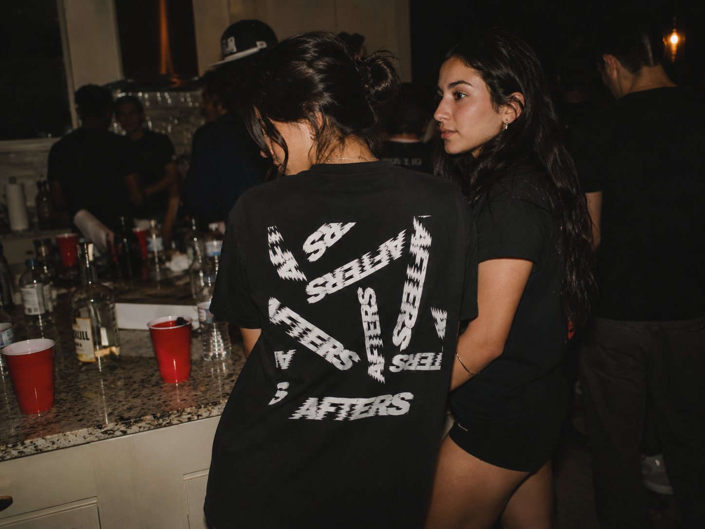Two friends at a kitchen counter with red cups wearing the Too Far Gone tee