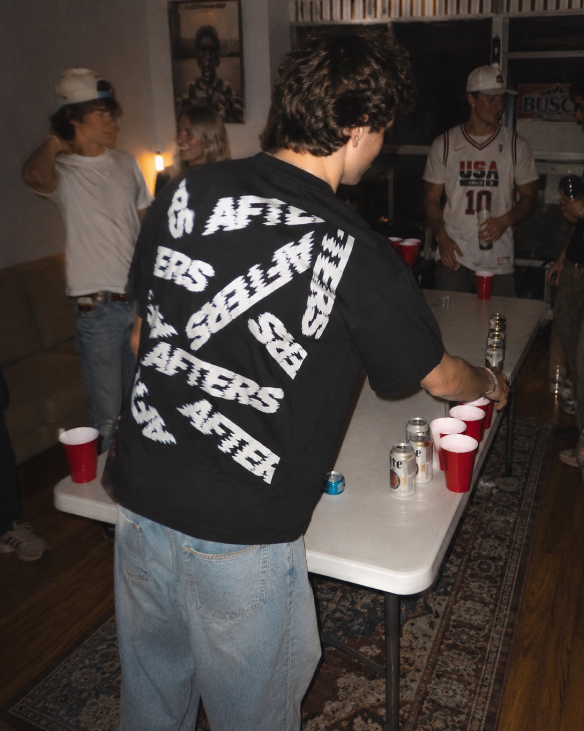 Man from behind in the scattered-AFTERS Too Far Gone tee playing beer pong at a house party