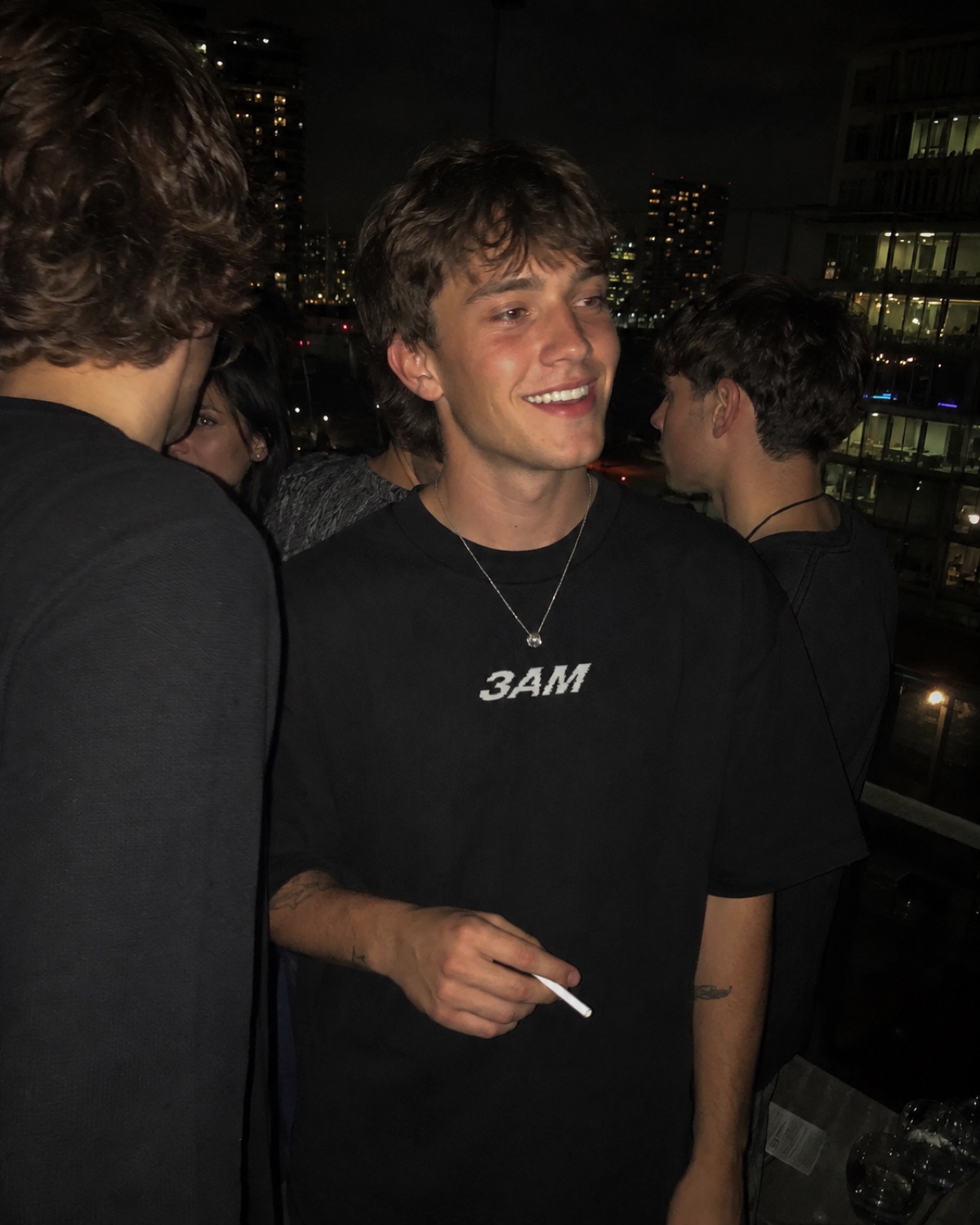 Guy in the 3AM tee at a rooftop party with the city skyline behind