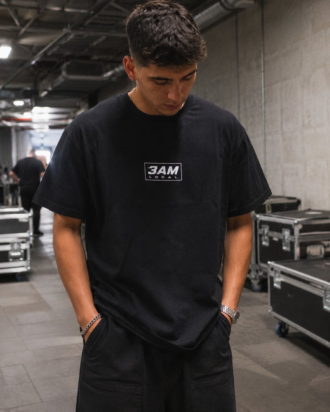 Man in the 3AM Uniform boxed-logo tee backstage among flight cases