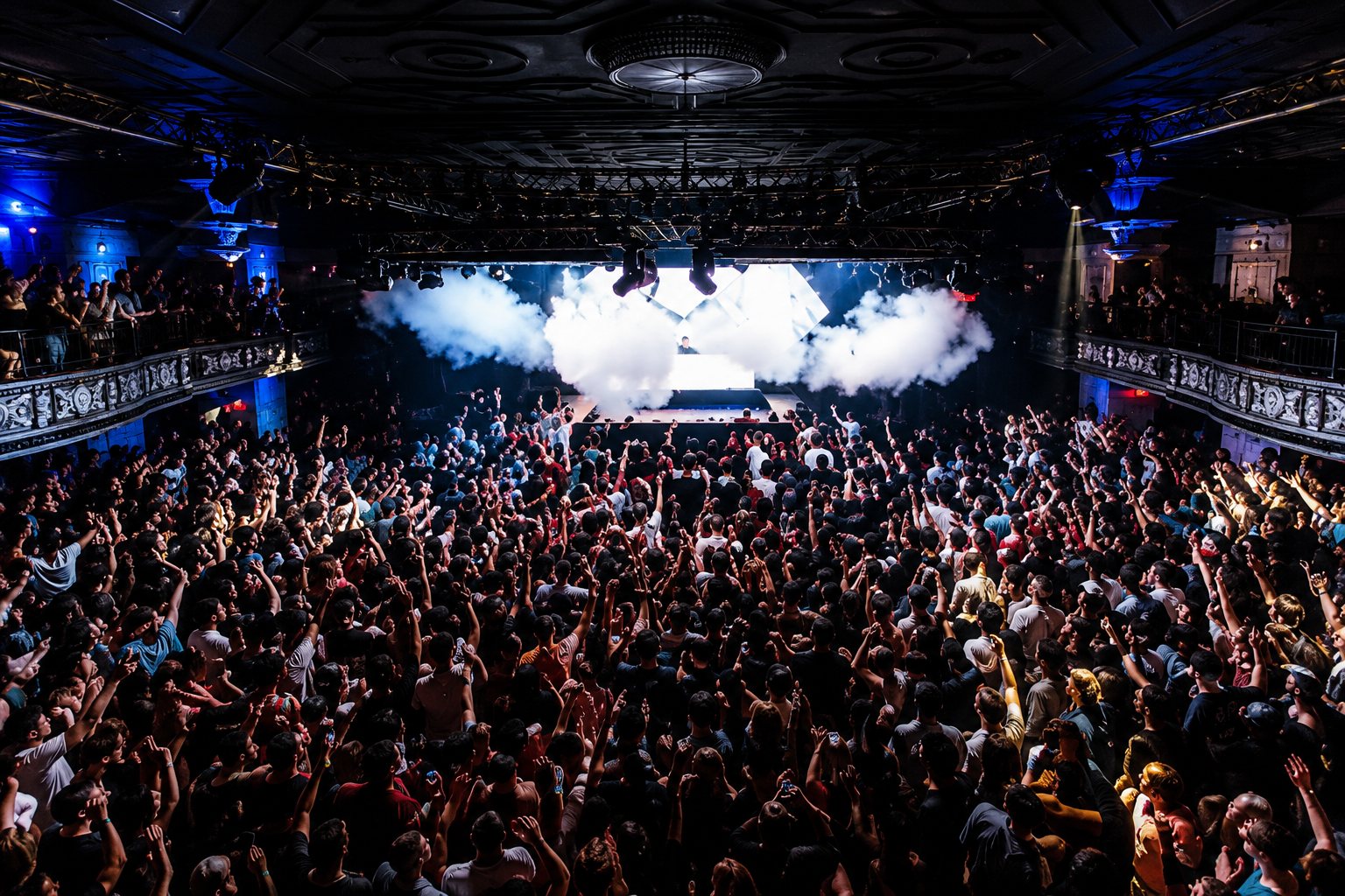 Packed Boston club crowd with hands up and CO2 jets under blue light