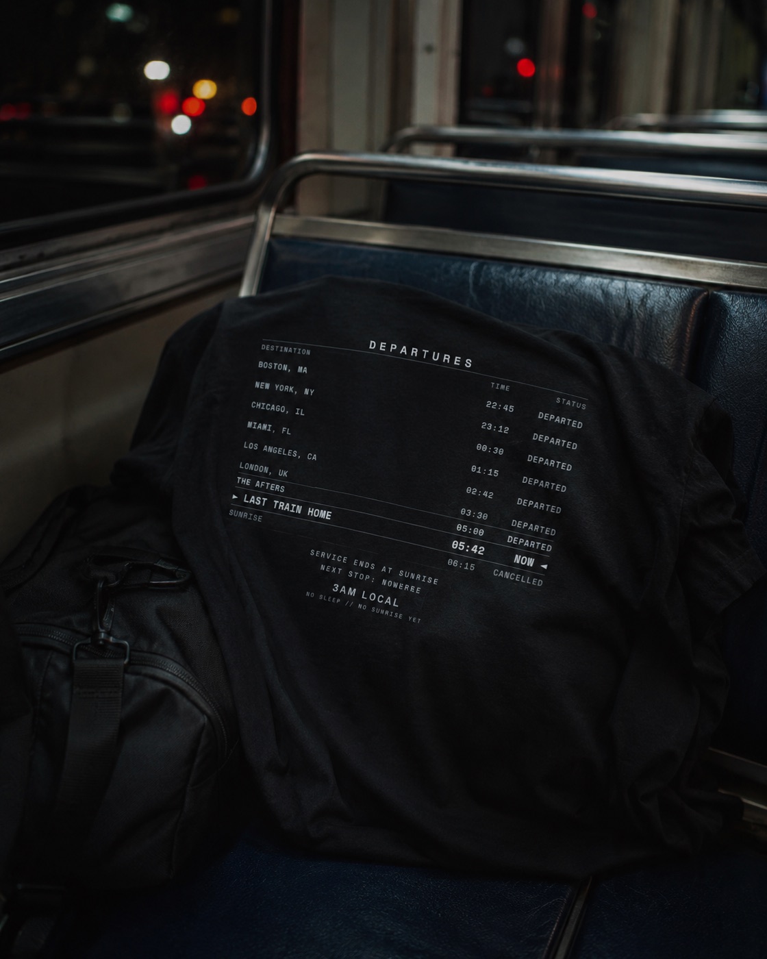 Last Train Home departures-board black tee laid across an empty late-night MBTA train seat