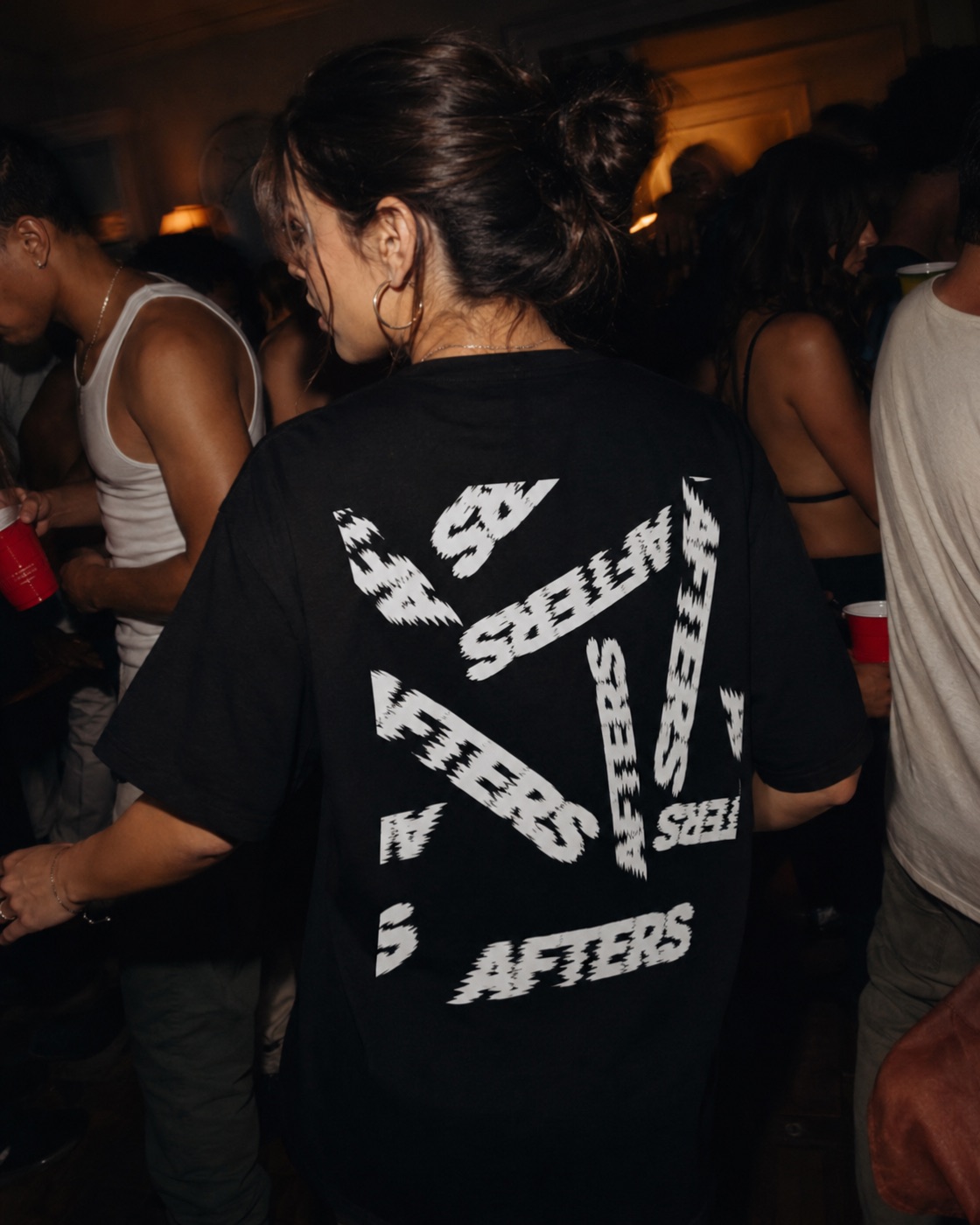 Back of the Too Far Gone scattered-AFTERS black tee at a packed house party